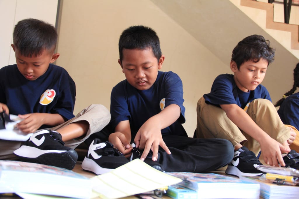 Muhammad Febrianto (center) is tying his shoelaces with his friends after receiving school supplies from XSProject.