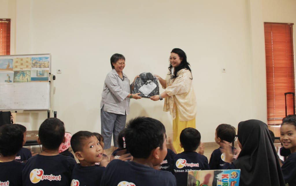 Retno Hapsari (left) receives symbolic assistance in the form of school supplies from Nina Amelina (right), representative of Kenvue Indonesia.