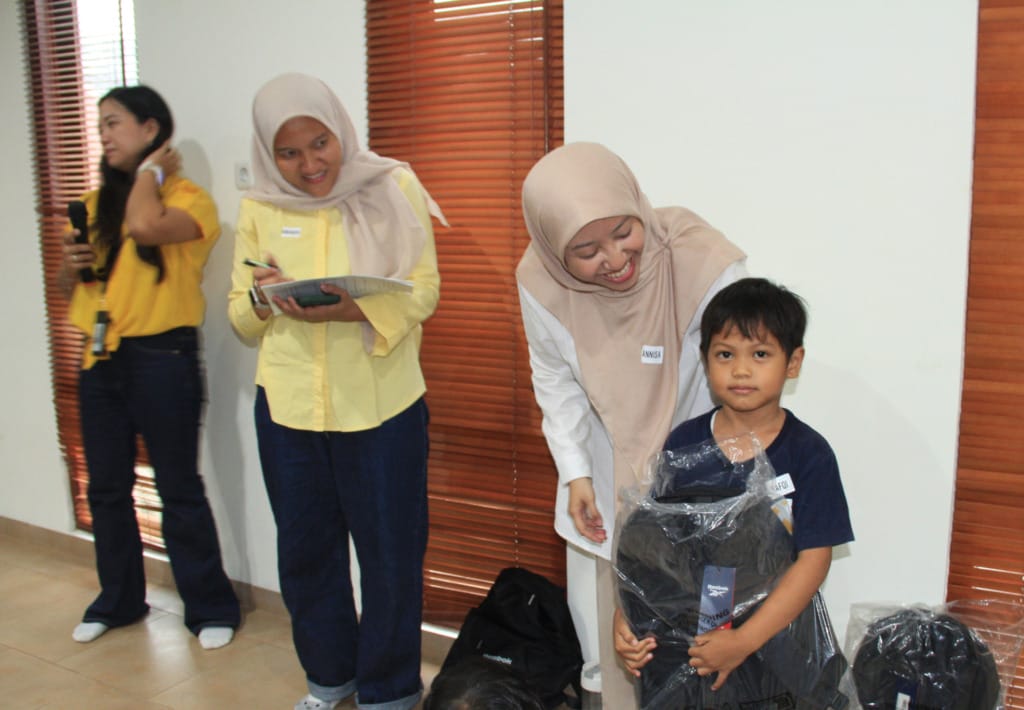 One of the children under XSProject's guidance receives a bag and school supplies from Kenvue Indonesia mentors.